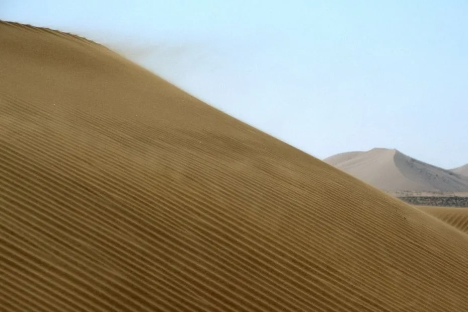 Sand dunes in the Badain Jaran Desert with tall, towering mounds under a clear sky.