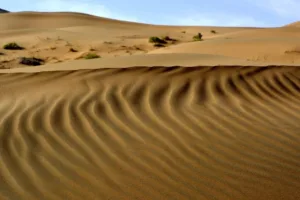 Sand dunes in the Badain Jaran Desert with small oasis lakes visible in the background.