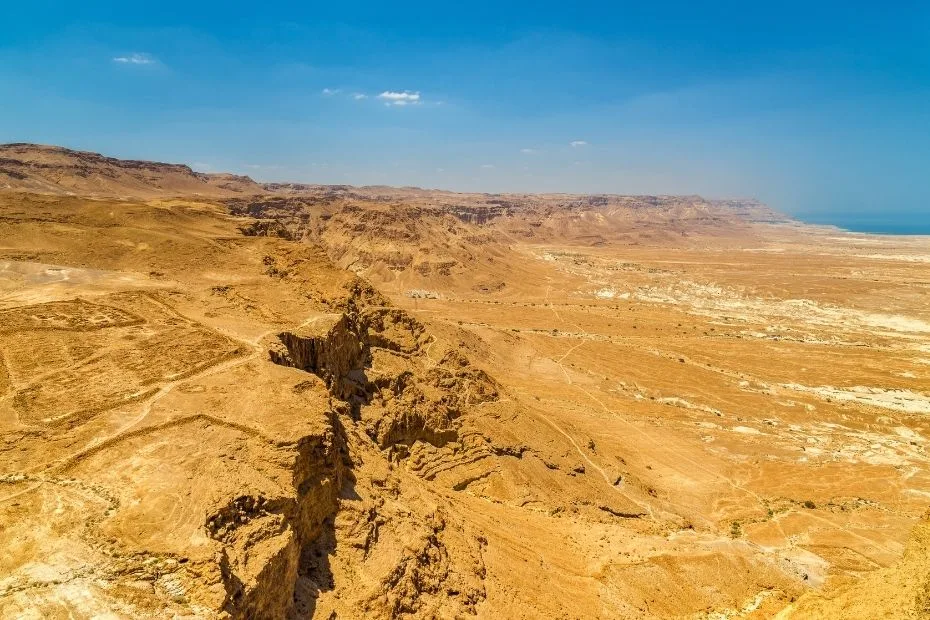 The rugged terrain of the Judaean Desert with dry, rocky hills and sparse vegetation.